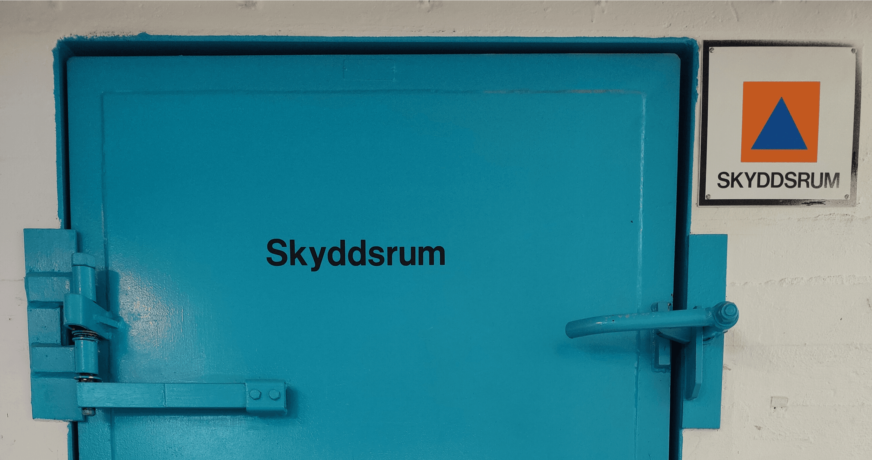 Beskuren bild av toppen på en blå metalldörr in till ett skyddsrum med text på dörren som säger "skyddsrum".